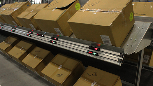 Light-directed put to store system with retail store cartons on shelving.