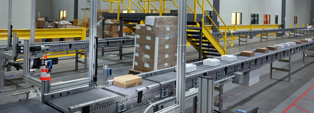 Conveyor moving several cartons and parcels through an RF scan tunnel to launch order completion automation.