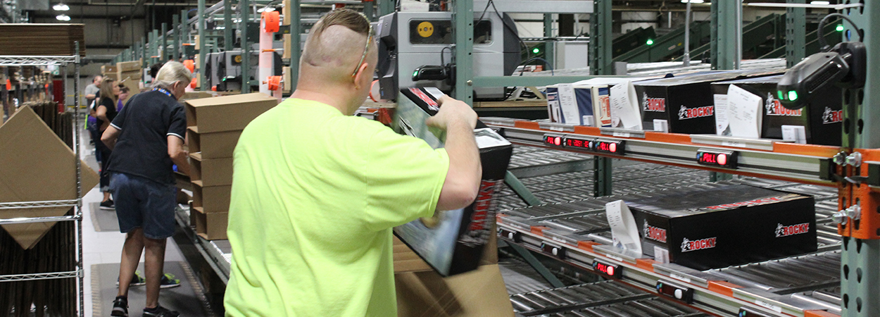 Line of distribution center employees using put walls to sort boxes of boots by light.